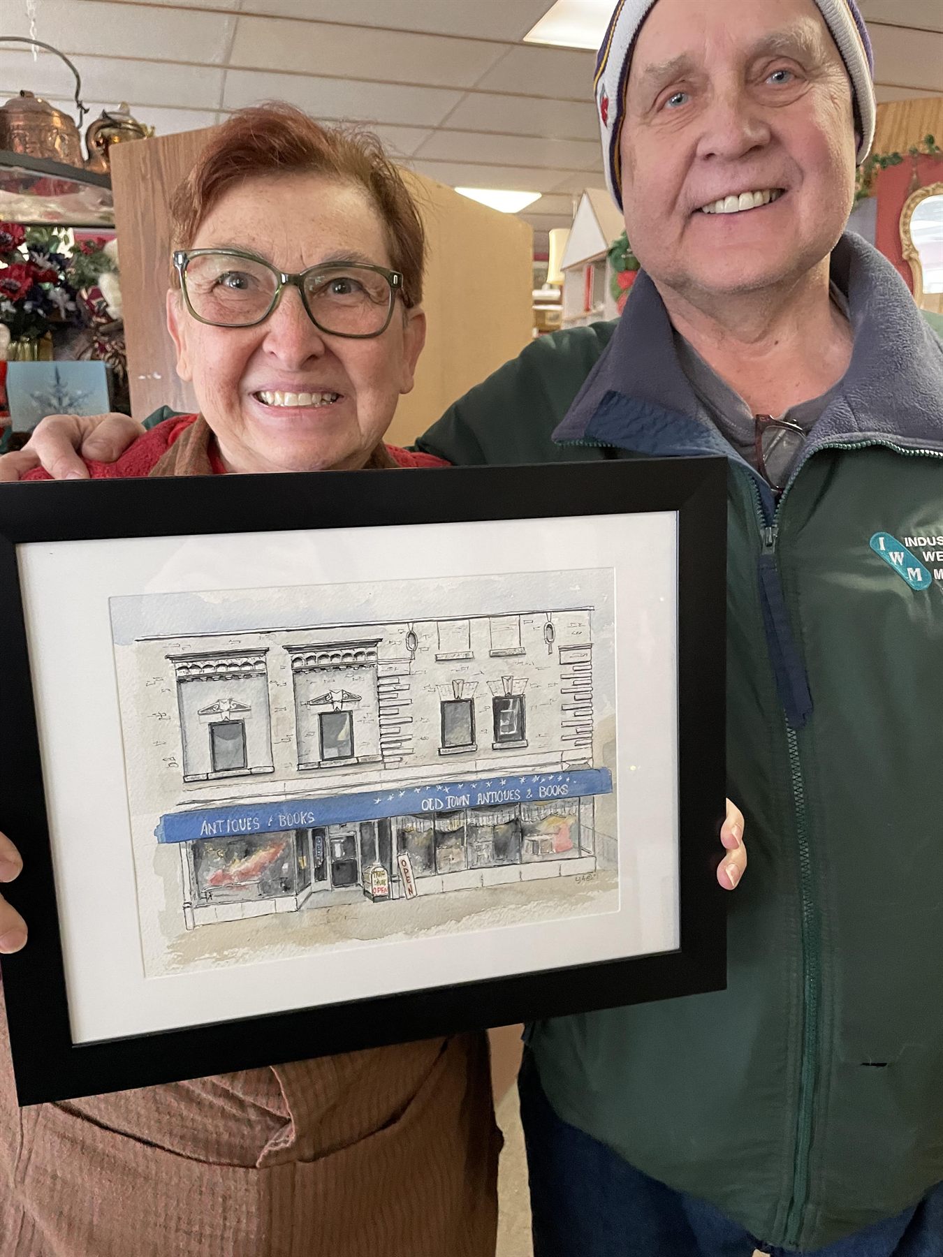 Carol and Dave holding a framed watercolor of the Old Town Antiques storefront.